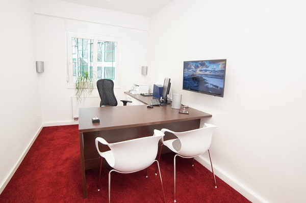 Modernes Büro mit Schreibtisch, zwei weißen Stühlen, Monitor und rotem Teppichboden.