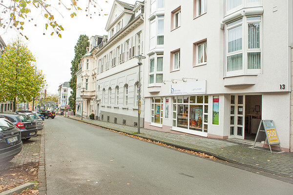 Moderne Fassade eines Physiotherapie-Zentrums an einer ruhigen Stadtstraße mit Parkplätzen.